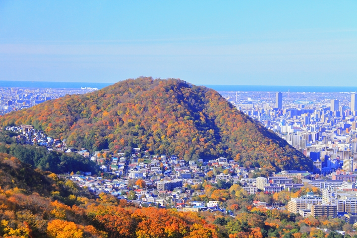 ▲遠方山頭撒滿秋意的「圓山」被高樓圍繞，就像1個掉在都市裡的巨大麻糬。　圖：中村昌寛さん／來源