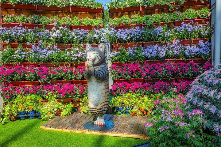 ▲朝隈俊男老師設計的「合掌貓咪」搭配花牆的映襯，除了有迎賓之意，更有向公園處苗圃同仁們表達感謝之意。　圖：臺北市政府工務局／提供