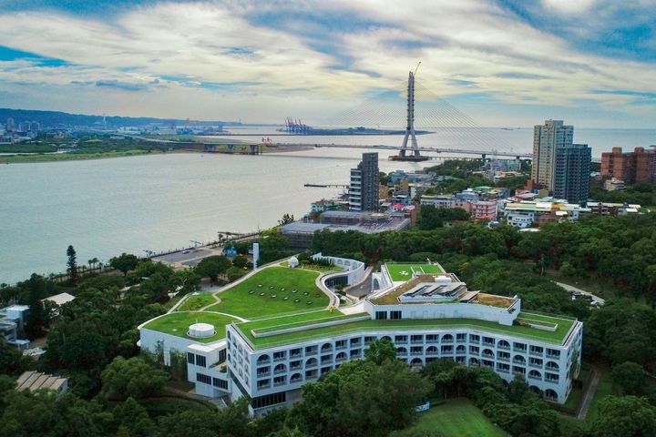 ▲從高空鳥瞰，酒店純白色的弧形建築與綿延的綠色屋頂花園，與淡水河畔、觀音山及興建完成的淡江大橋構成絕美的山海線條。　圖：淡水將捷金鬱金香酒店／提供
